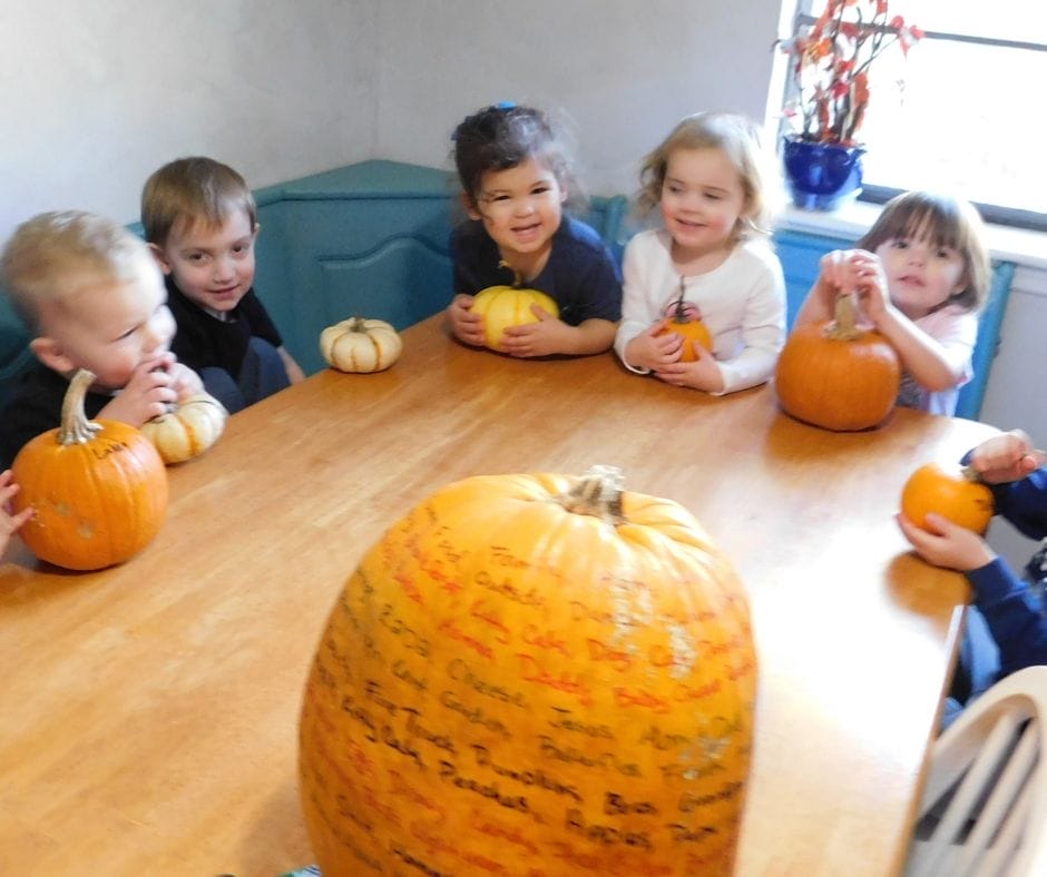 kids sitting around table with pumpkins and big pumpkin with things they are thankful for written on it.