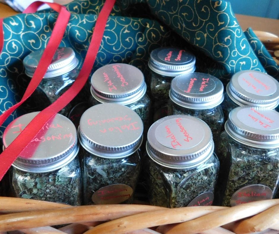 jars of homemade italian seasoning in a basket with green fabric and red ribbon