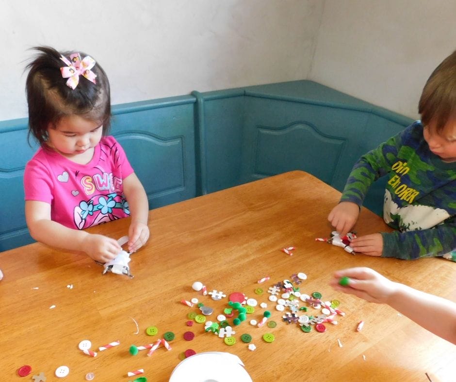 kids at a table decorating christmas ornament twig stars with beads, buttons, pom poms and assorted things
