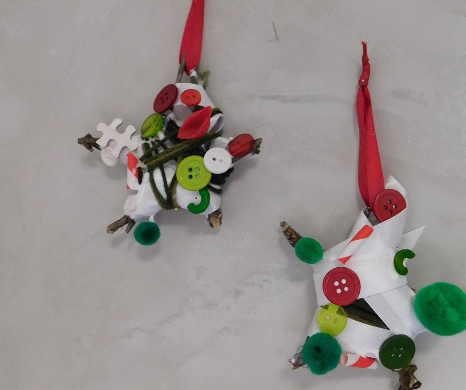 finished twig star oranaments decorated with ribbons, yarn, buttons and assorted red, white and green findings and hanging on the wall on a nail.