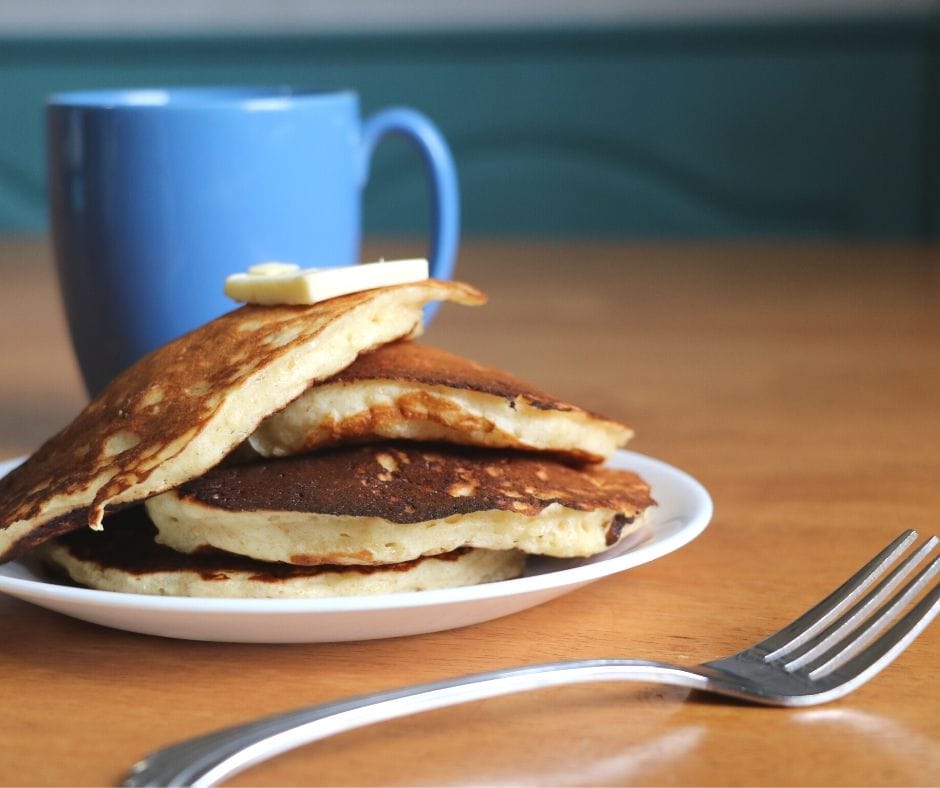 healthy pancakes piled on a plate with butter on top and a cup and fork