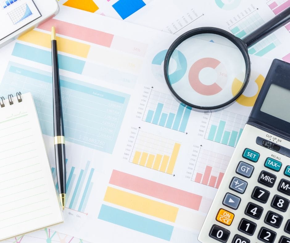 Spreadsheets, graphs and paperwork with magnifying glass, pen, and calculator.