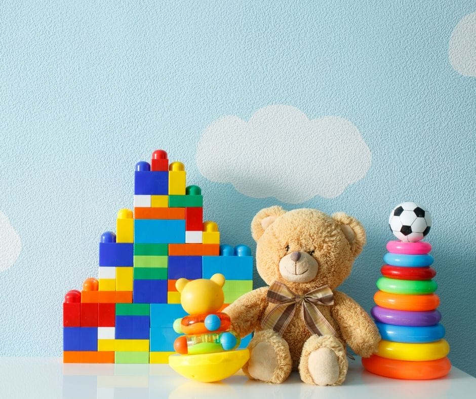Brightly colored kids toys on a shelf - blocks, rings and a stuffed bear. 