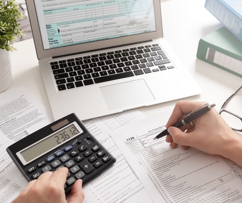 Tax paperwork, calculator and laptop with a person filling out forms. 