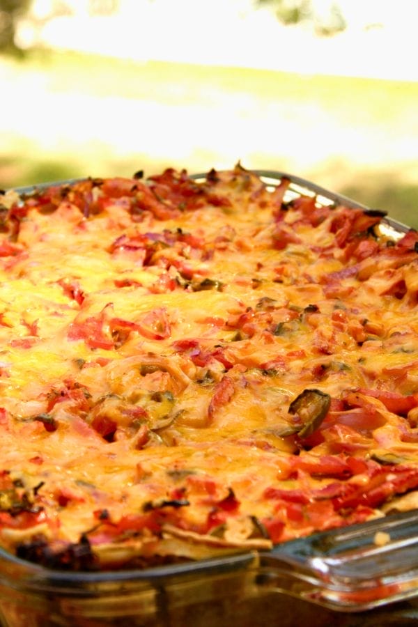 A glass baking dish filled with baked pasta topped with melted cheese, tomato sauce, and savory chunks of pork roast.