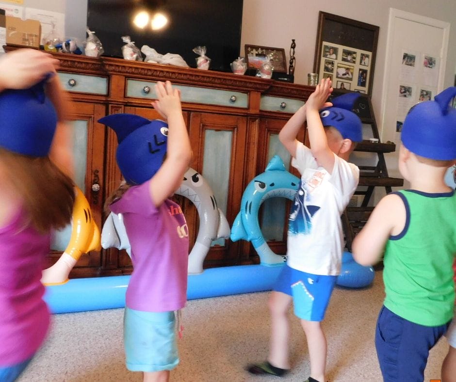 kids playing with shark hats, singing and making shark fins on top their heads