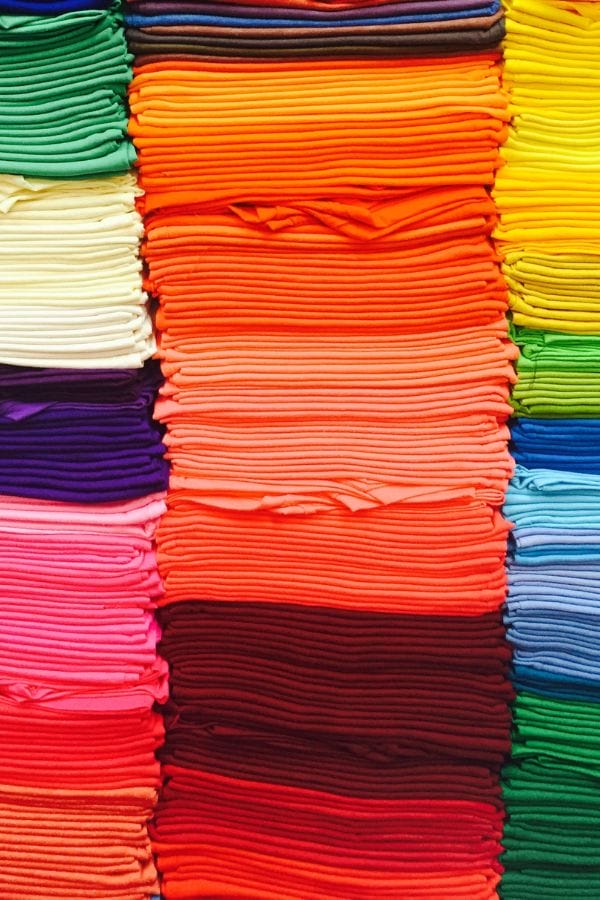 Stacks of folded fabric in various vibrant colors, including orange, pink, yellow, green, and blue, arranged neatly—perfect for crafting cheerful child care T-shirts.