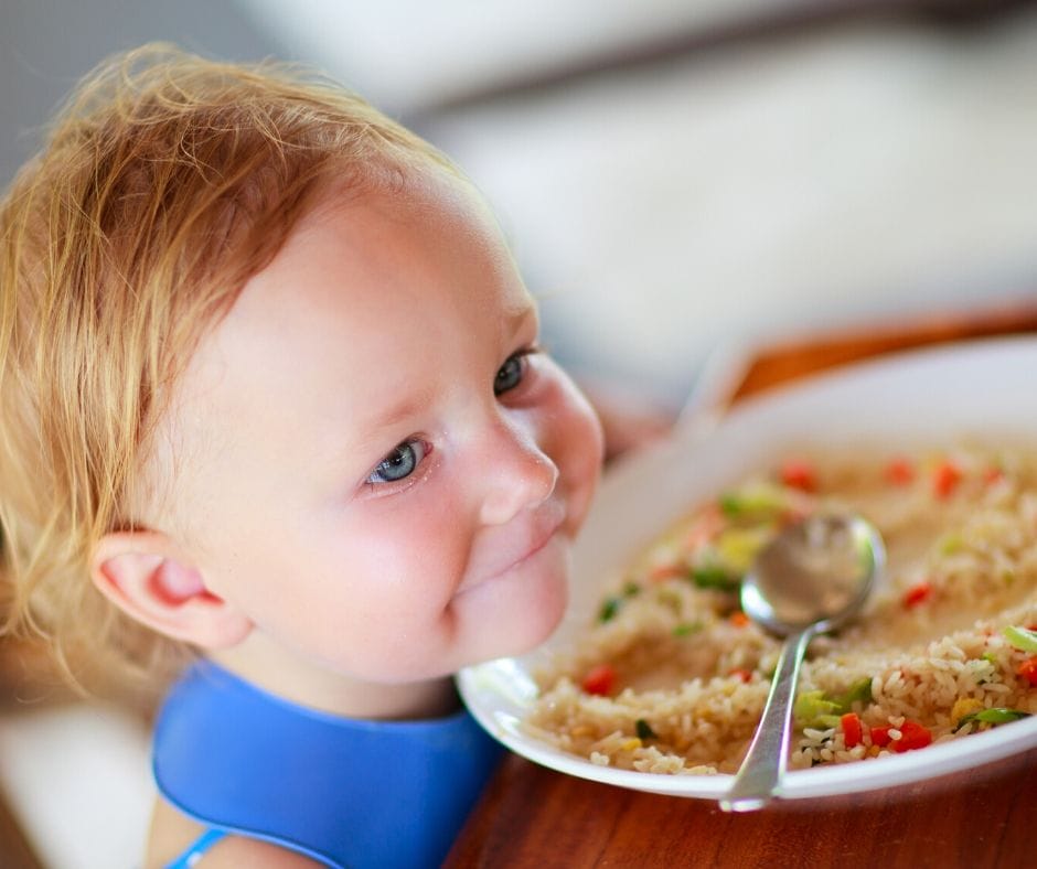 child at the table with plate of rice and vegetables 