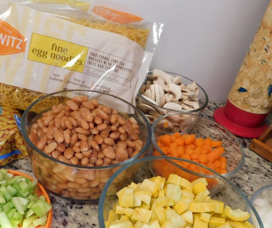 ingredients for summer squash soup on the counter, beans, celery, yellow squash, carrots, mushrooms, and noodles 