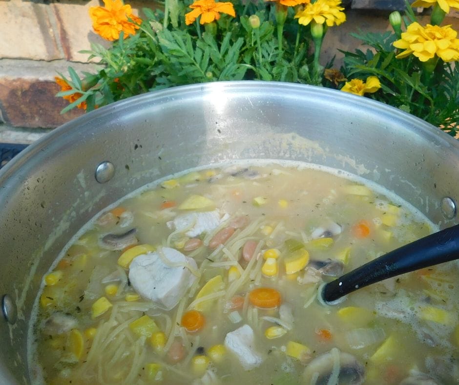 big pot of summer squash soup on the table with marigolds and brick behind