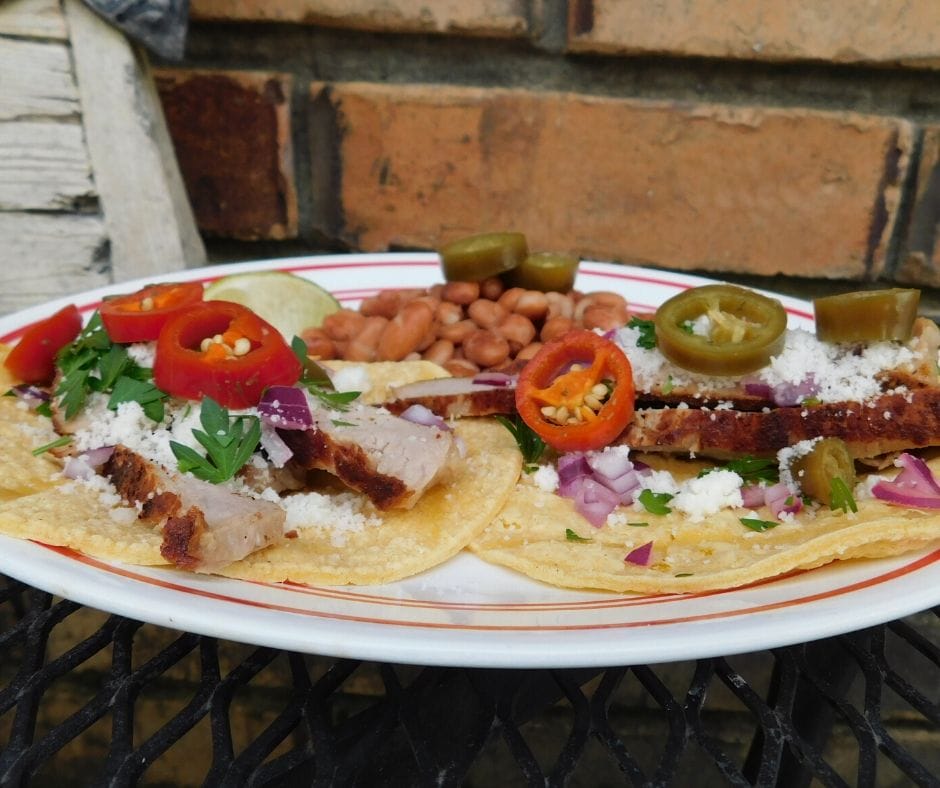 Pork chop tacos on a plate with a side of beans.
