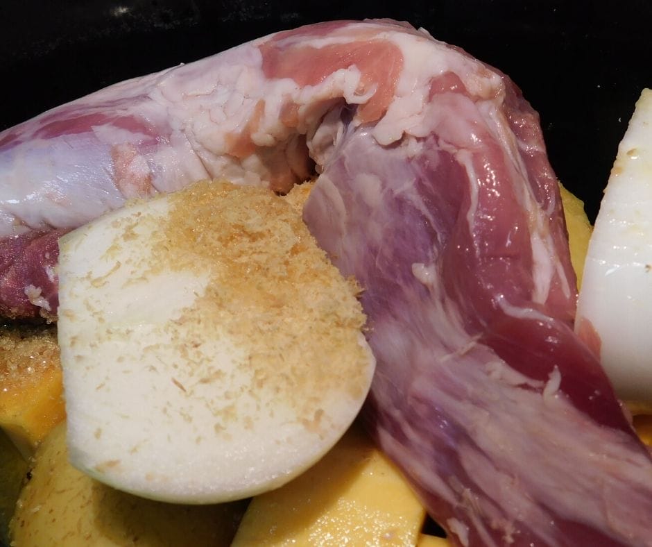 raw pork tenderloin over vegetables with seasonings going into the crock pot