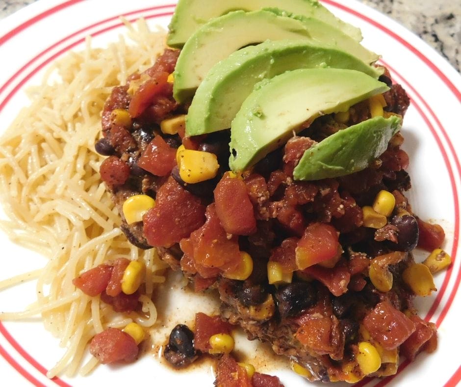 slow cooker pork chops with rotel, corn, and black beans topped with avocado slices and a side of pasta