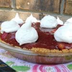 strawberry pie with whipped cream dollops on top of a flowered towel sitting outside on a table