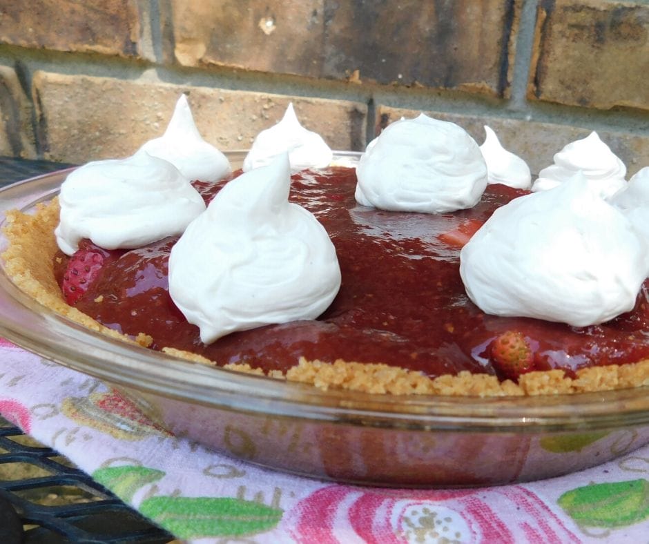 strawberry pie with whipped cream dollops on top of a flowered towel sitting outside on a table