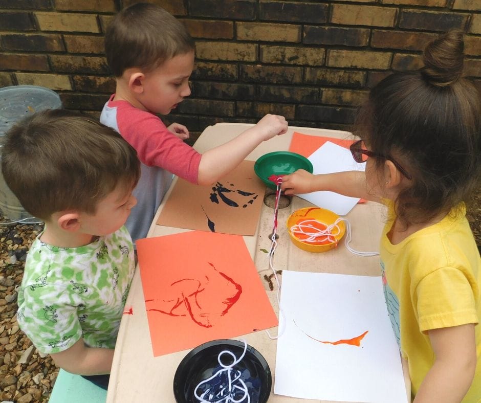 kids painting on an outside table with yarn