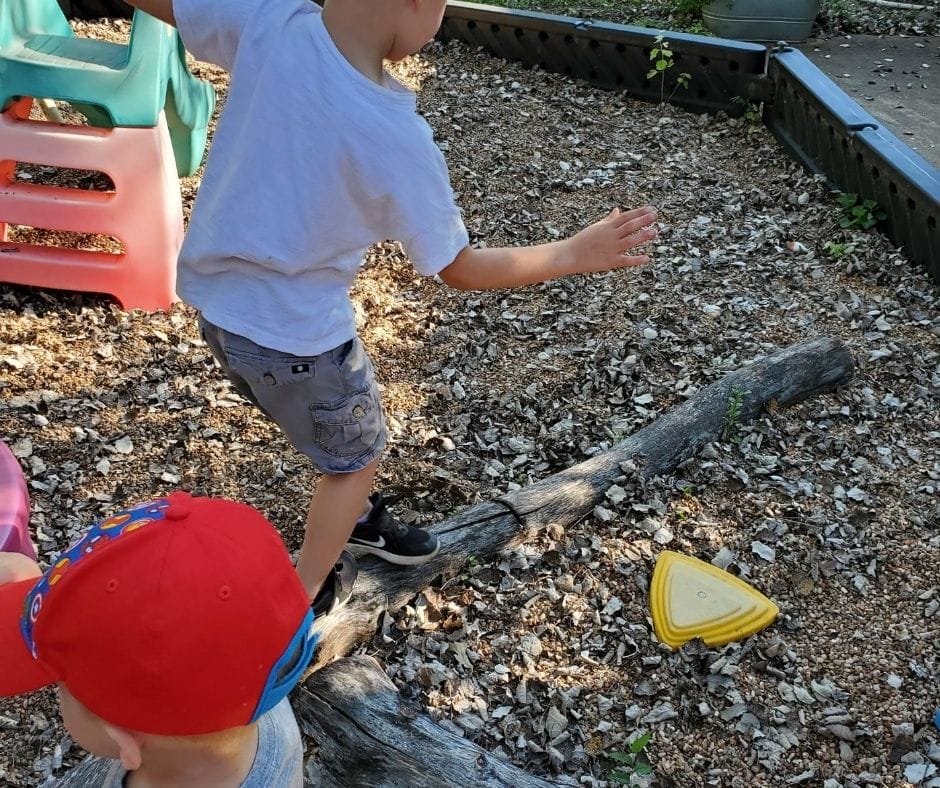Kids playing on home daycare playground, walking along logs for balance