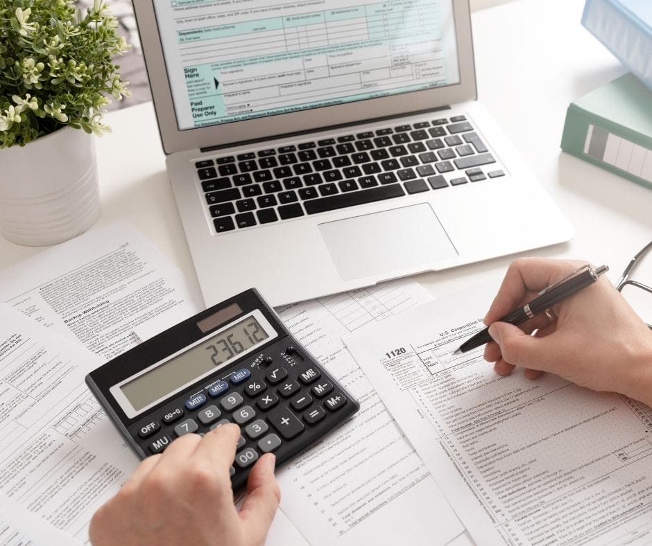 person figuring taxes with calculator and laptop as well as tax forms.