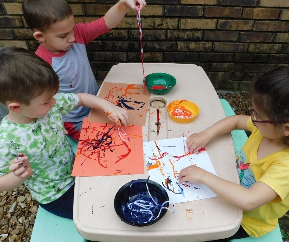 kids painting with yarn on a picnic table