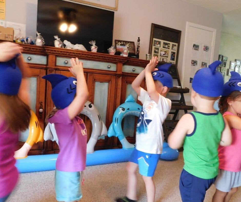 Kids singing baby shark and dancing wearing shark hats in home daycare