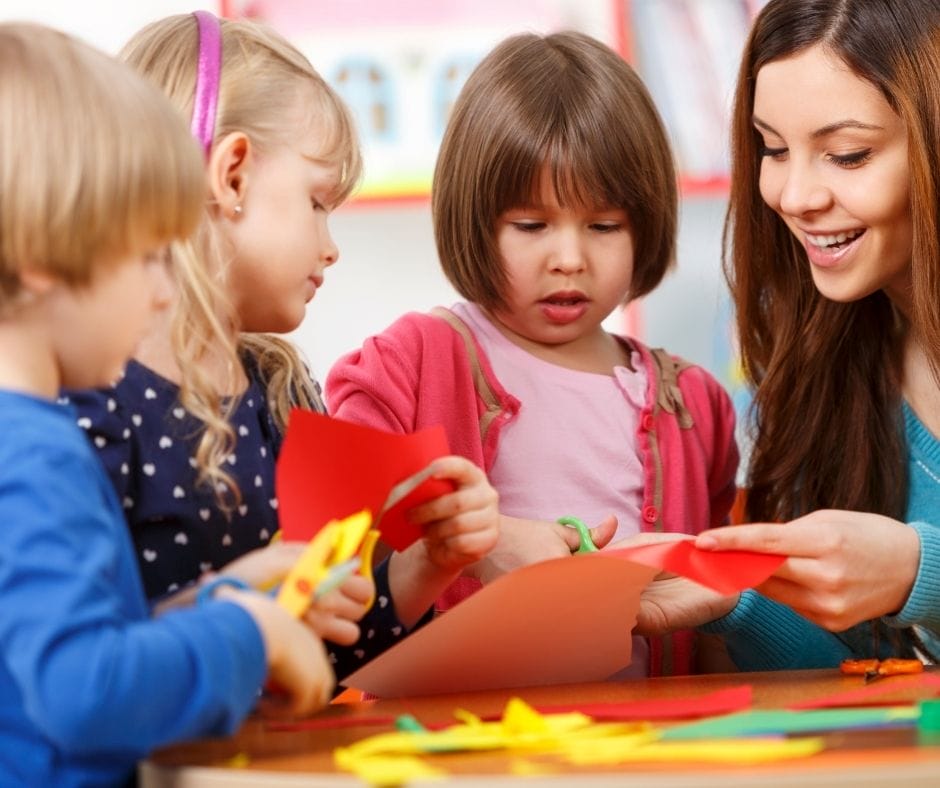 Kids playing with paper and scissors with their home daycare provider.