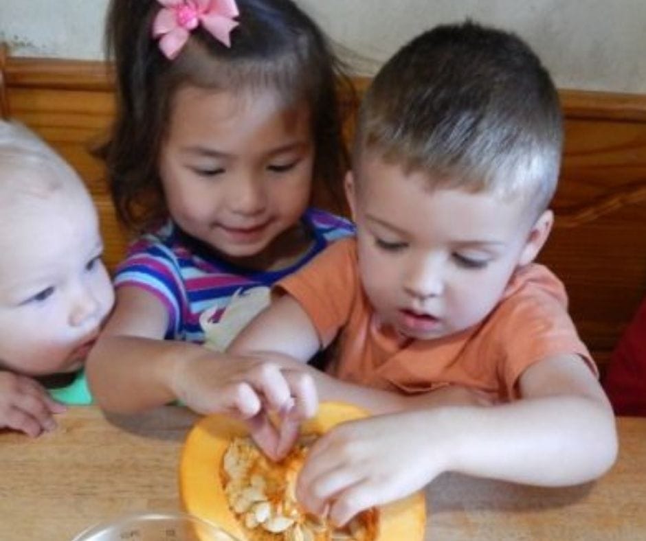 kids exploring pumpkin guts in home daycare at the table