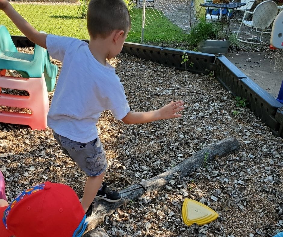 child balancing on log in the play yard.