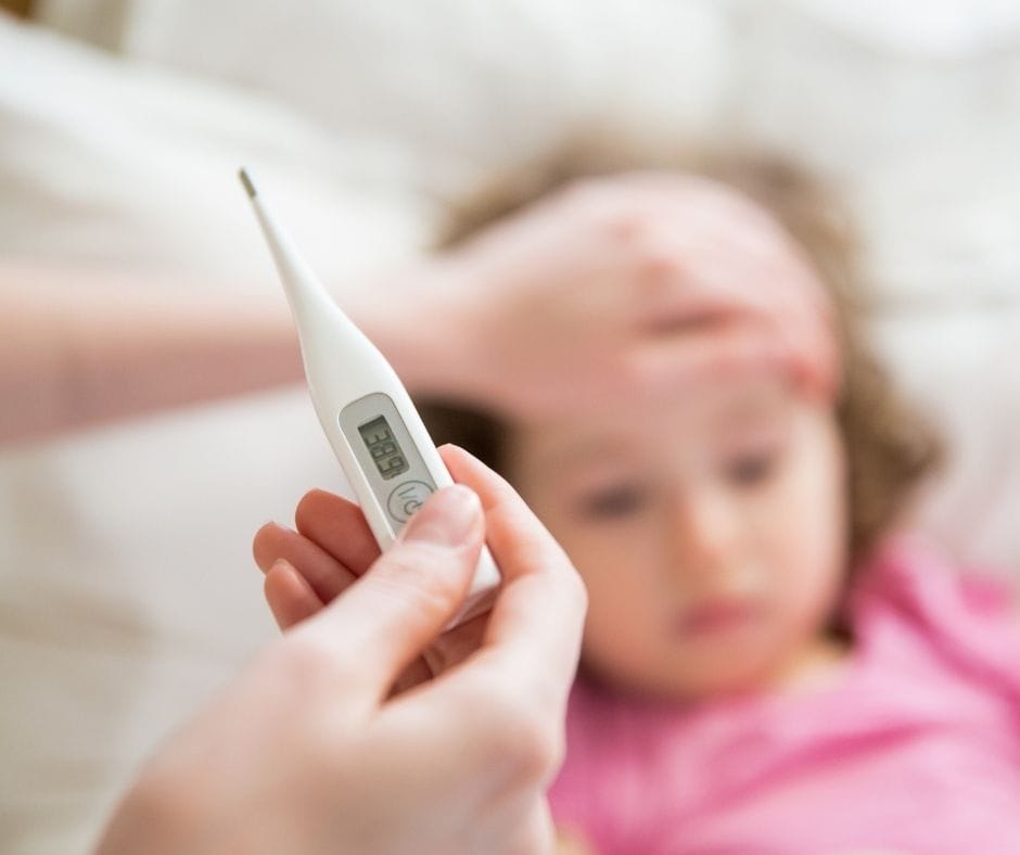 sick child in bed with mom holding thermometer
