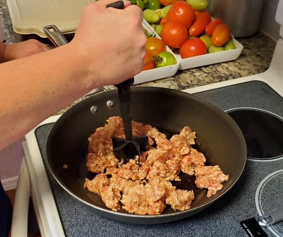 cutting up and cooking sausage in a skillet on the stove
