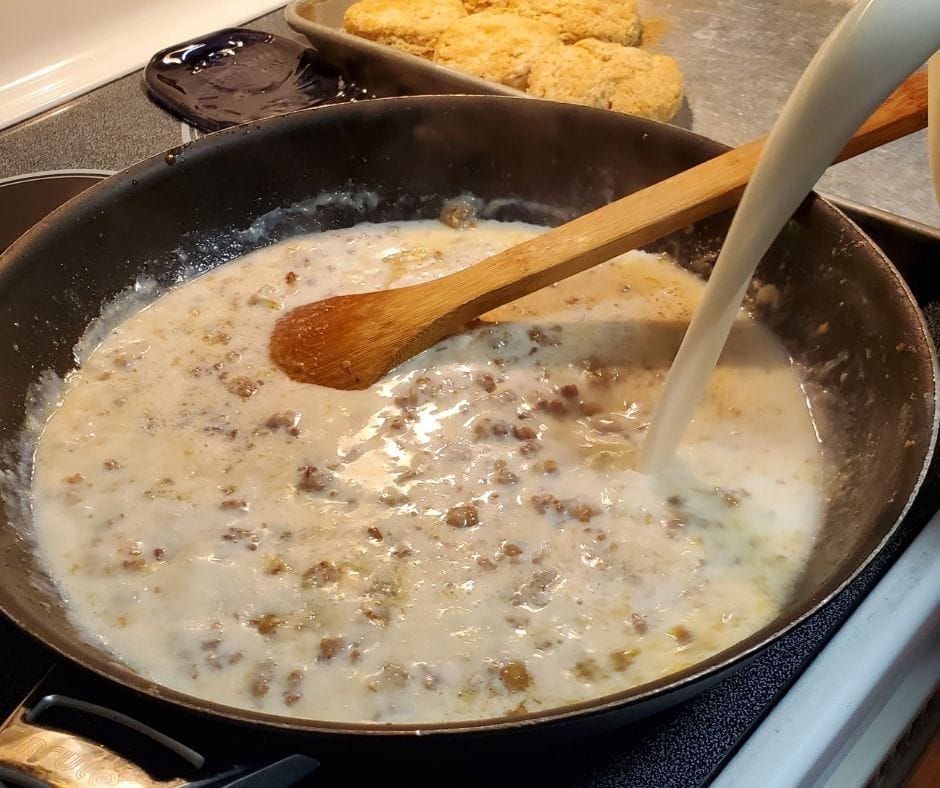 pouring milk into sausage gravy in skillet on the stove