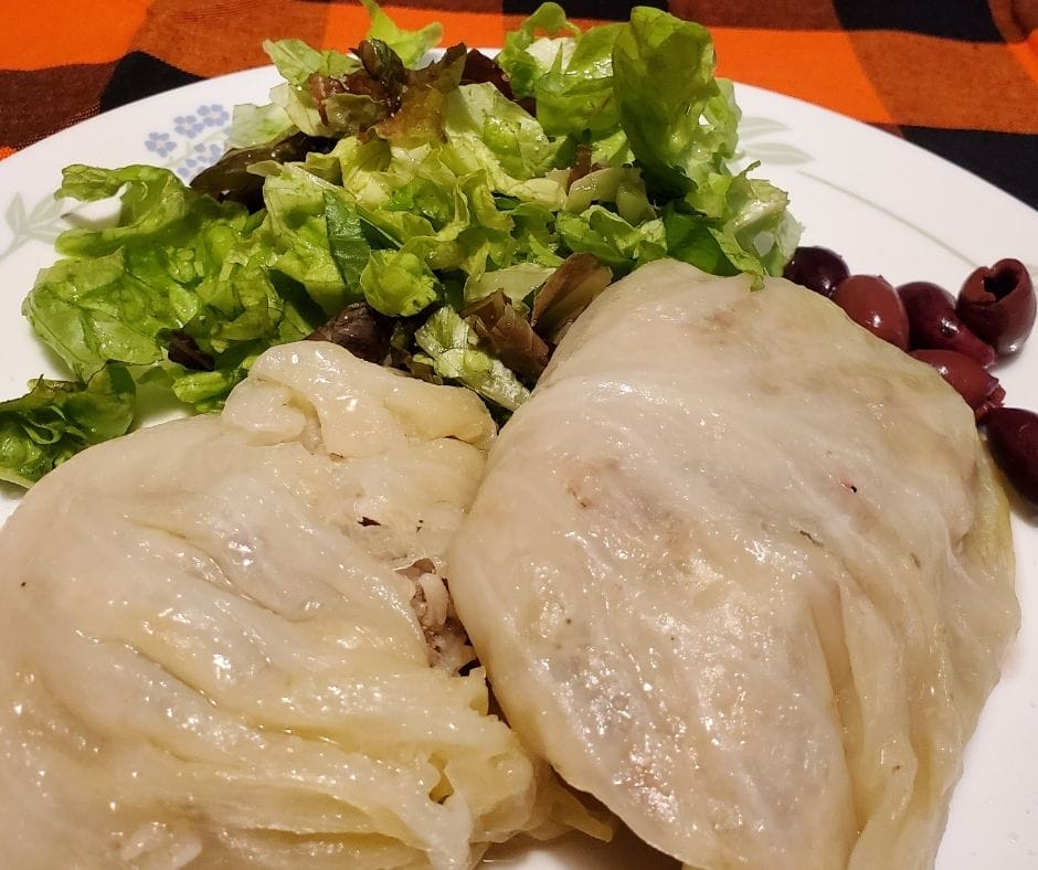 sausage cabbage rolls on a plate with salad and olives