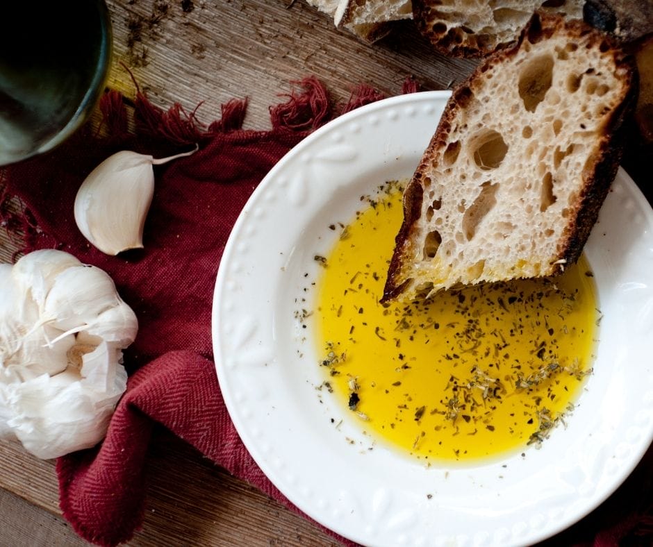 bread on a plate with bread dipping oil made with garlic bread sprinkle on a board with a towel and some garlic