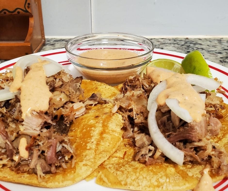 leftover pork carnitas on a plate with onions and chipotle ranch drizzle and a few lime wedges