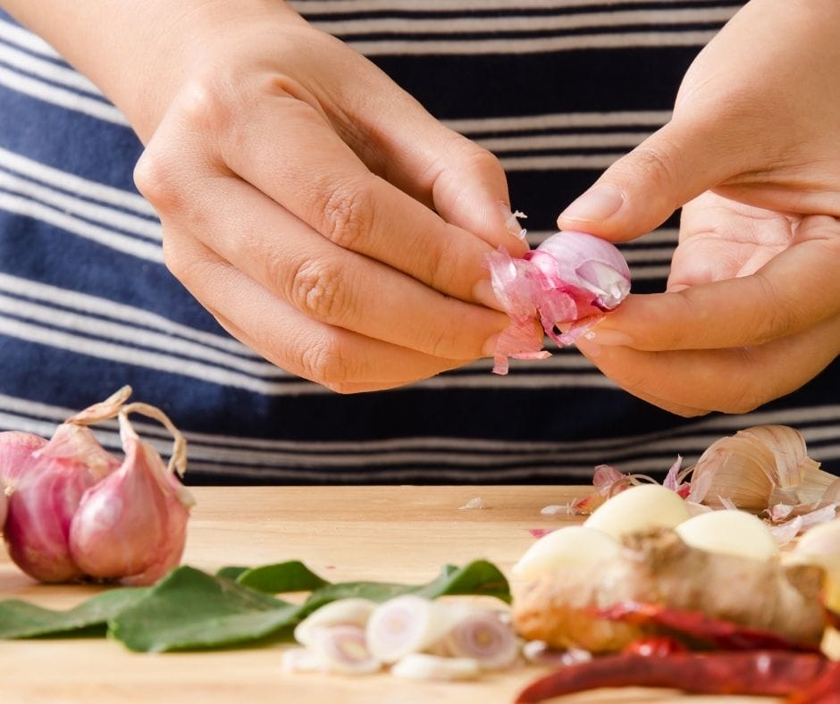 someone peeling shallots on a cutting board with some other vegetables, garlic and sliced shallots