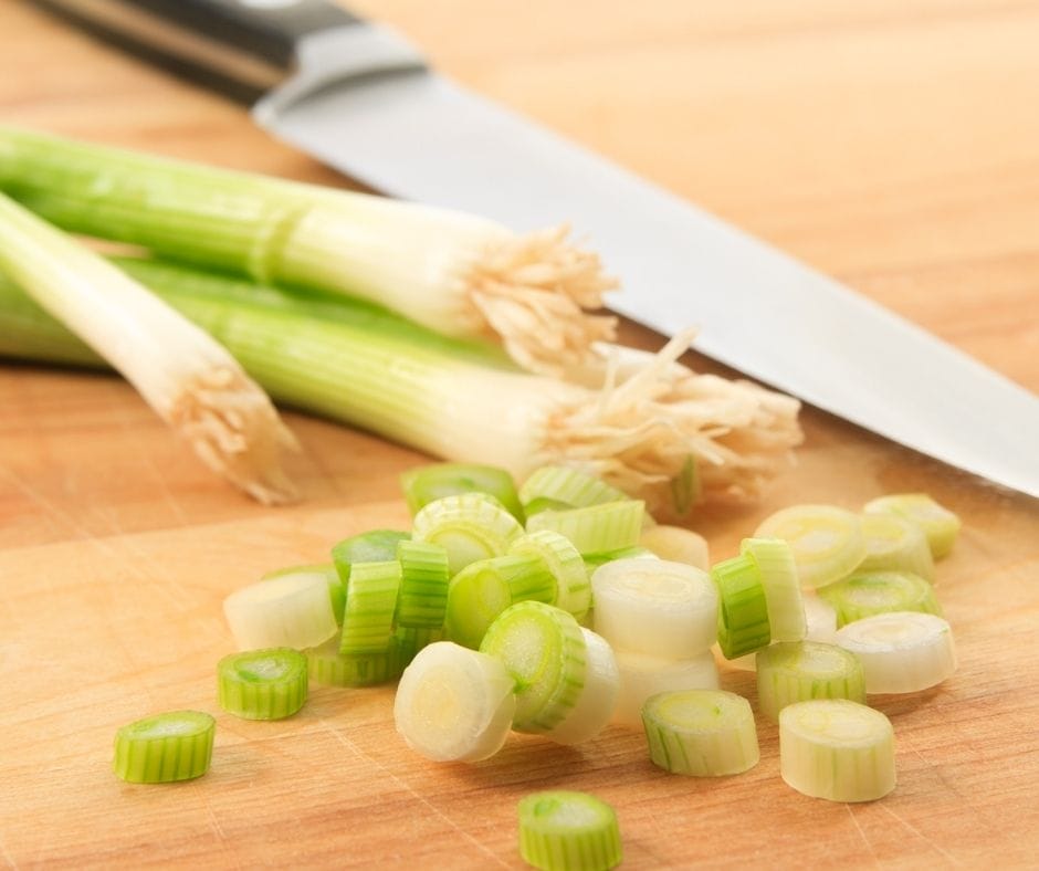 green onions or scallions sliced on a cutting board with a knife laying