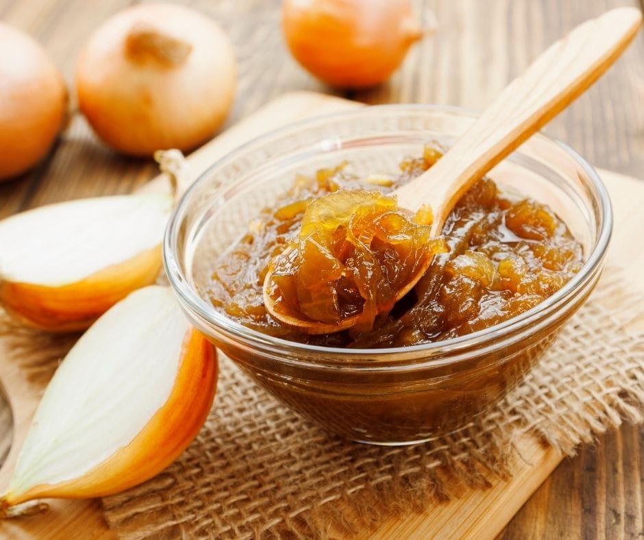 carmelized onoins in a bowl on a cutting board with a spoon full on top and whole and halved onions around the bowl
