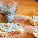garlic compound butter spread on some bread on a cutting board with a jar of garlic bread seasoning mix behind it
