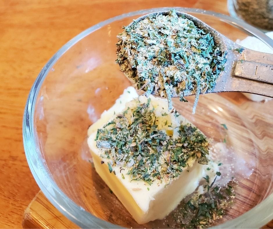 Garlic bread seasoning in a measuring spoon over a bowl with a big block of butter in it.