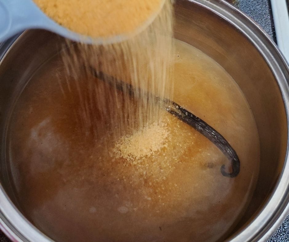 pan of water with vanilla beans and raw sugar pouring in to make homemade vanilla syrup for coffee drinks and more.