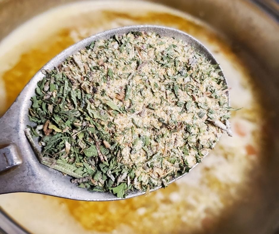 garlic bread seasoning in a measuring spoon over sausage spinach tortellini soup in a pot