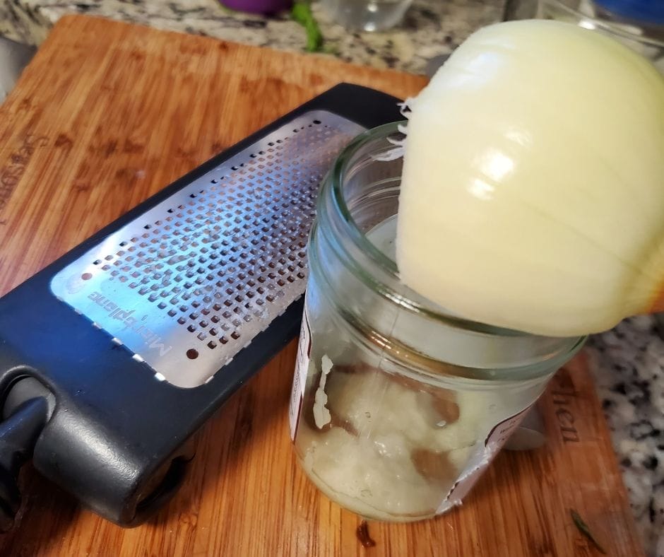 an onion over a jar with a fine grater next to it for grating onion into balsamic dressing.