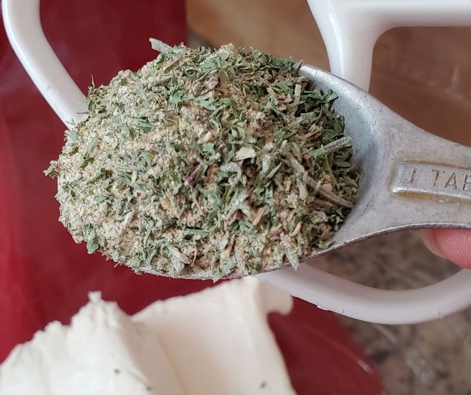garlic bread seasoning mix in a spoon over a bowl of cream cheese