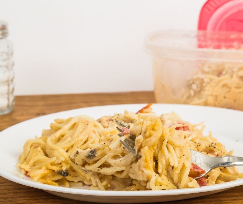 leftover chicken in pasta on a plate on a table with a container of chicken behind