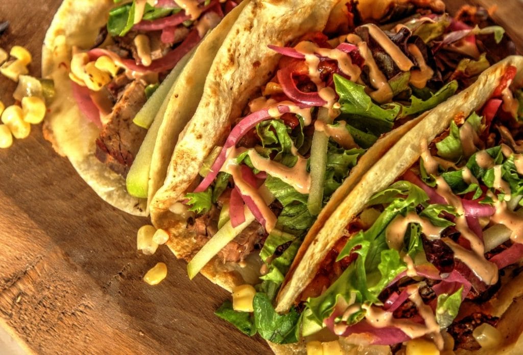 three crunchy tacos with brisket , lettuce, and sauces.
