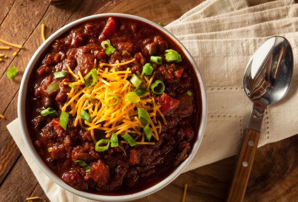 Bowl of brisket chili topped with cheese and scallions on a napkin