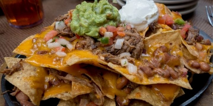 tall plate of brisket nachos with cheese, onion, tomatoes, guacamole and sour cream