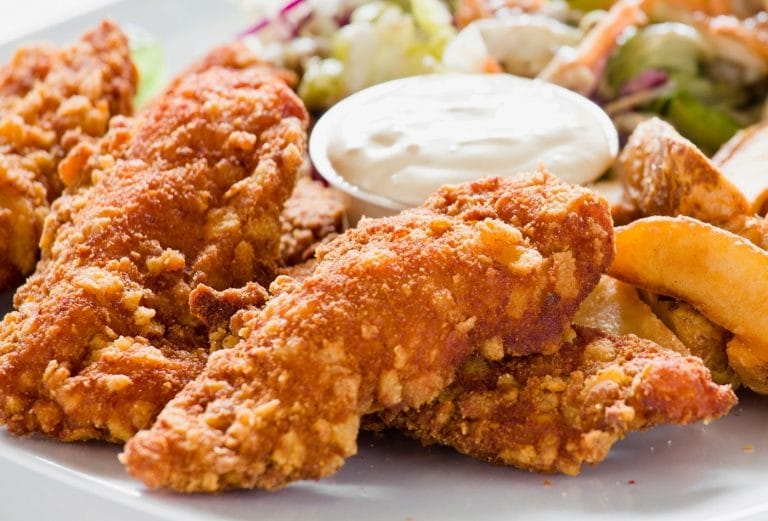 crispy chicken breast tenders on a plate with sauce and salad