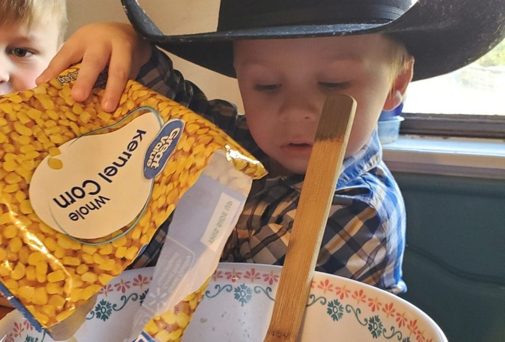 child in a cowboy hat pouring corn into a bowl to make elote in a cup