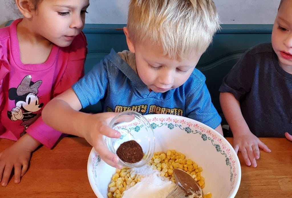 a child pouring chili powder into elote in a cup recipe 
