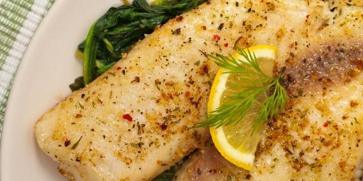 Air fried fish fillets on a plate with greens topped with lemon slices and dill sprigs